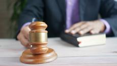 Man's hands show on bible and gavel at a table