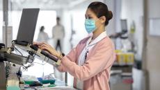 A nurse checking on a patient's record in a hallway laptop computer