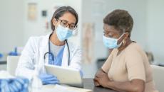 Masked doctor showing tablet to masked patient