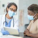 Masked doctor showing tablet to masked patient