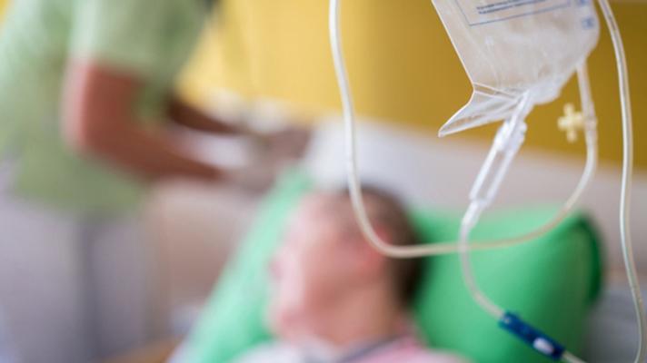 Infusion bag in foreground with patient and infusion nurse in background