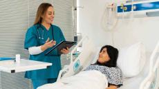 Doctor with clipboard talking to patient in hospital bed