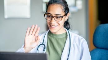 Doctor smiles and waves into a laptop during a telehealth visit