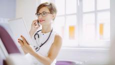 A doctor reviewing a patient's record on a digital tablet while answering a phone call