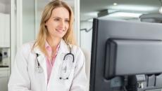 A doctor reviewing a patient's file on a desktop computer